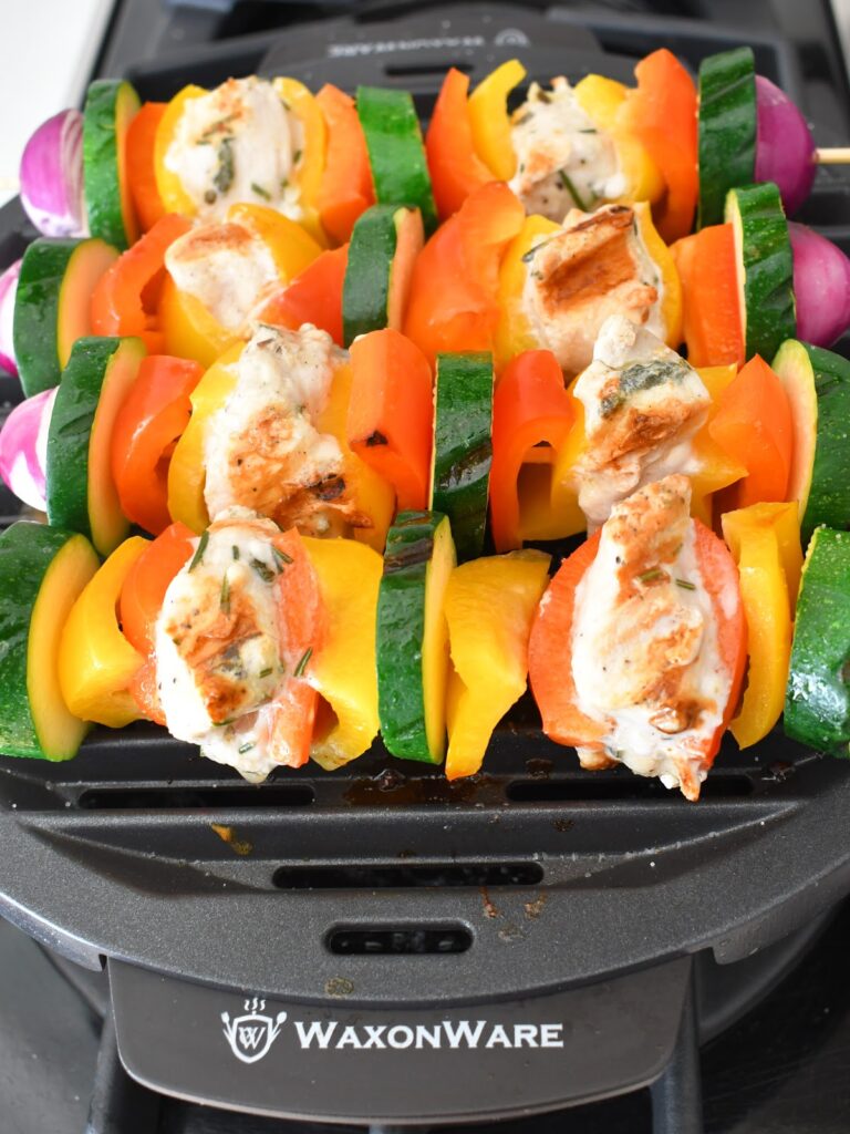 Colorful vegetable and chicken skewers with zucchini, bell peppers, onions, and grilled chicken pieces cooking on a WaxonWare grill.
