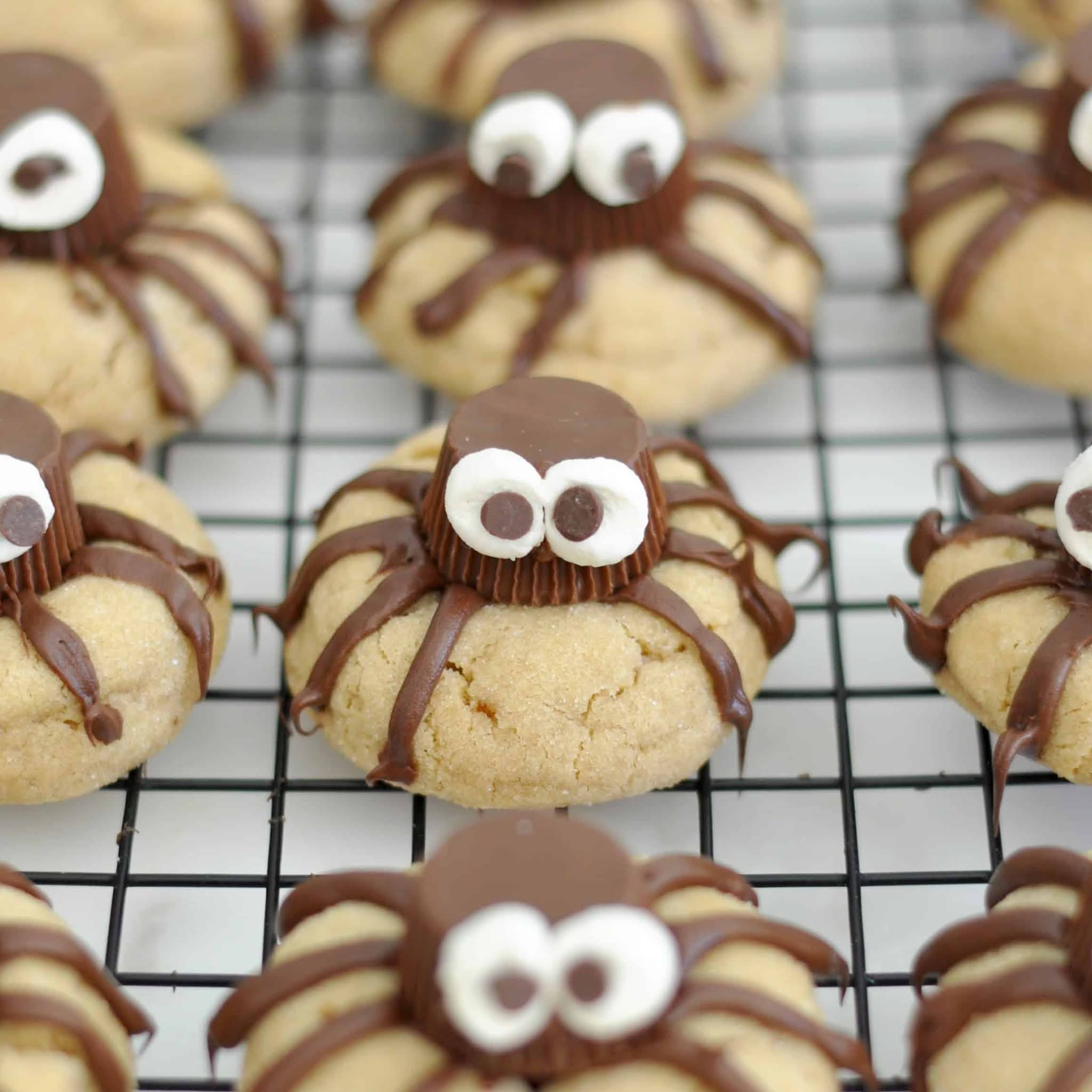 Peanut butter cookies decorated as spiders with chocolate candy bodies, candy eyes, and chocolate legs, arranged on a cooling rack.