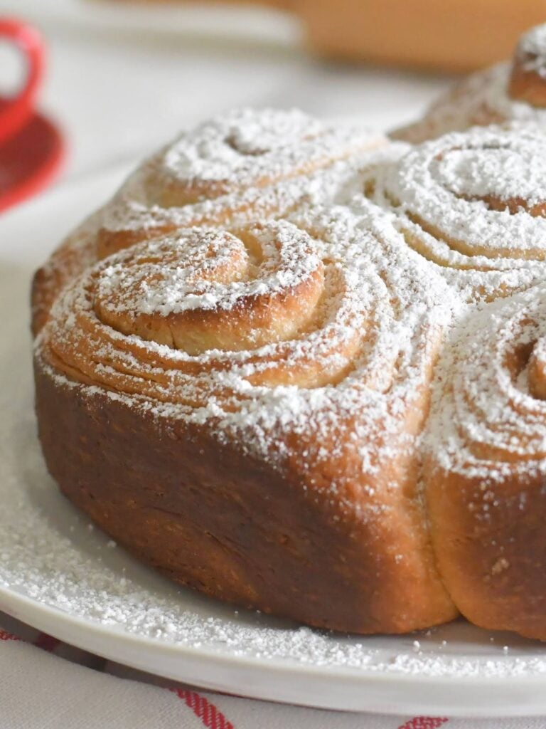 A close-up of golden-brown cinnamon rolls dusted with powdered sugar, arranged in a circular pattern on a white plate.